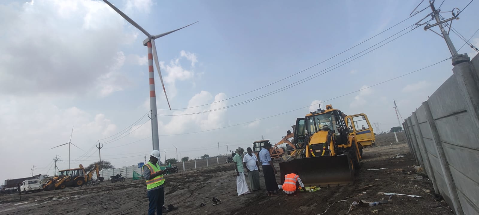AARAA Infrastructure team during groundbreaking ceremony for 180 MWp Solar Power Project in Tuticorin, Tamil Nadu, with heavy machinery and wind turbines in the background.
